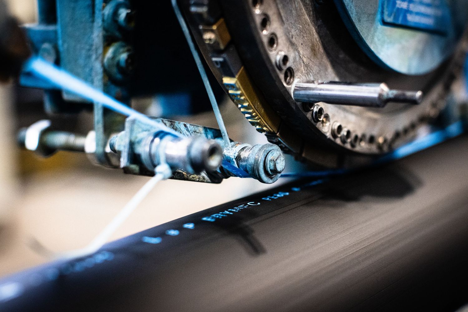 Close-up macro shot of a machine transferring bright blue labels from blue tape to a large black HDPE pipe.