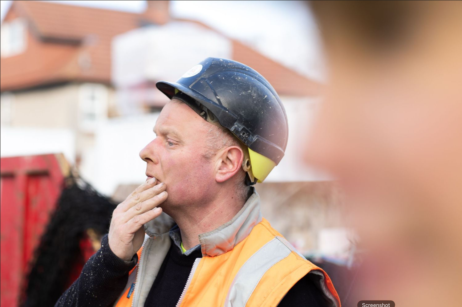 A person wearing a baseball cap blows a whistle while standing outdoors.
