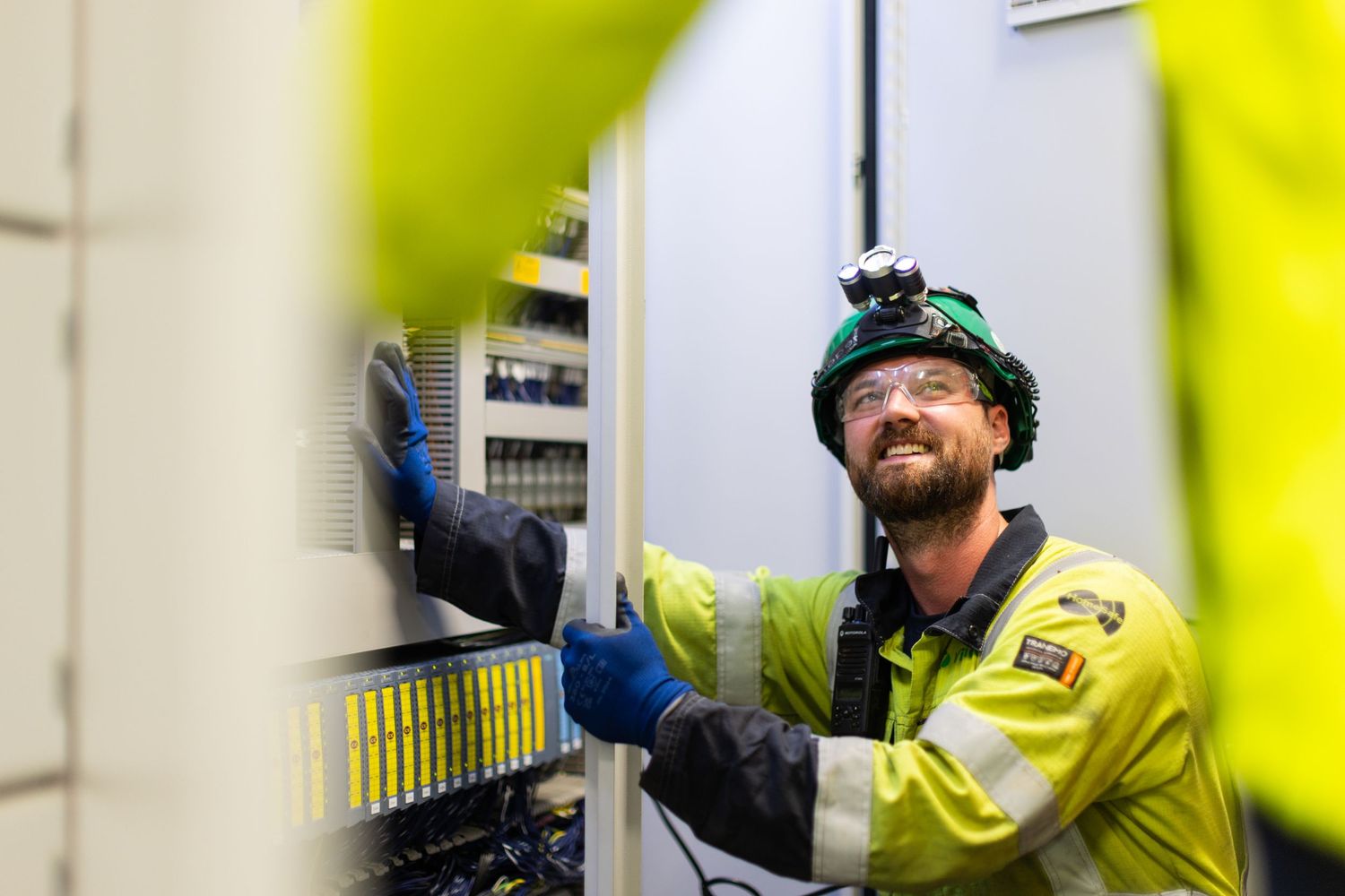 Industrial worker in high-visibility safety gear and hard hat operates control panel at manufacturing facility.