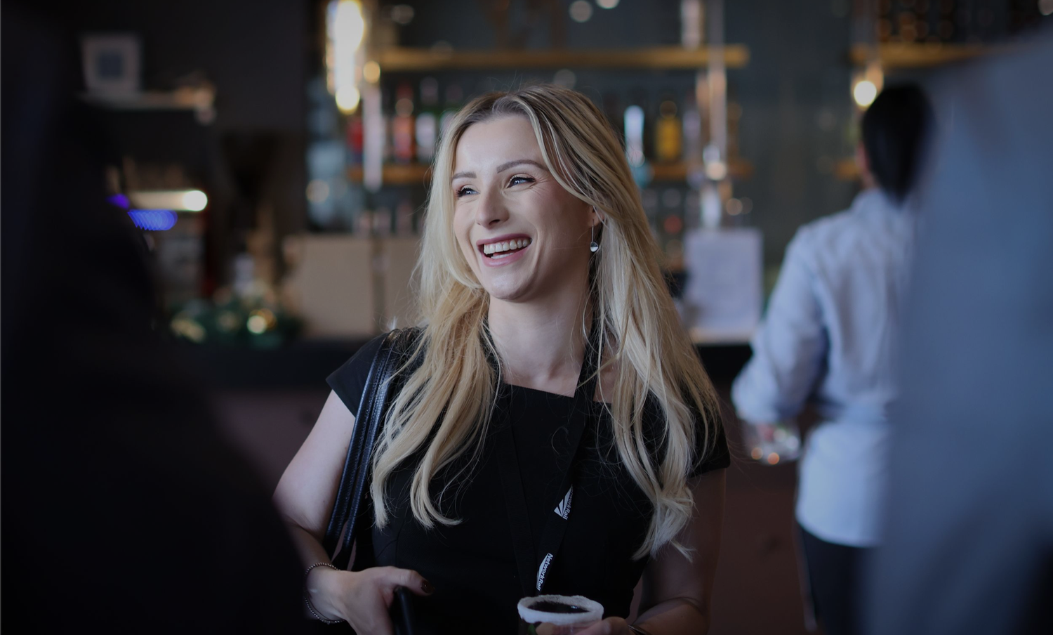 A person smiling and laughing while sitting at a table in a restaurant setting.