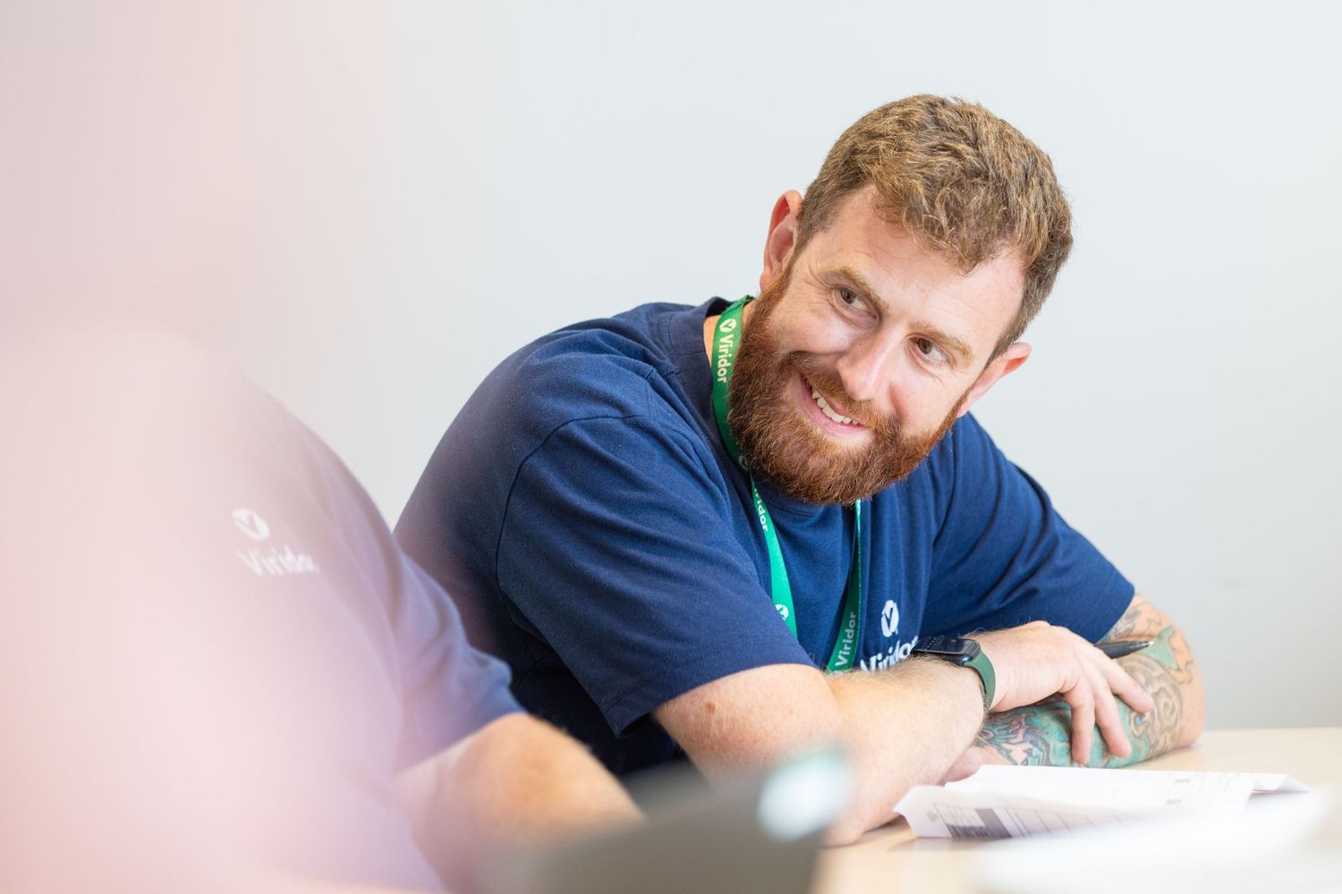 Someone wearing a blue shirt writes on paper while working at a desk in a bright office setting.