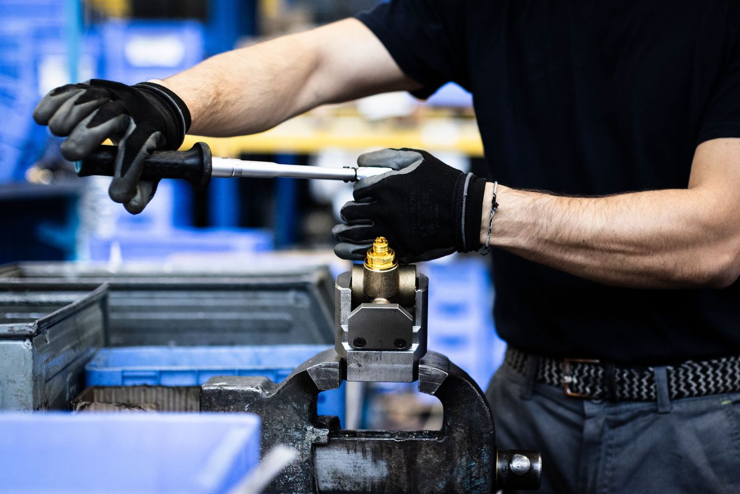 A close-up view of hands working with a precision wrench to tighten a valve casing in a manufacturing facility.