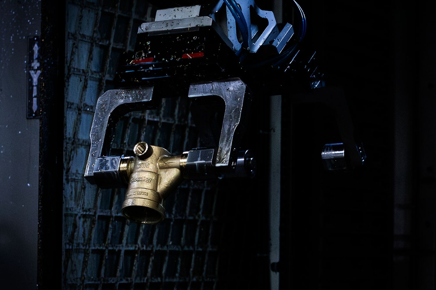 A dramatic dark scene shows a robotic arm carrying a freshly forged brass valve casing.