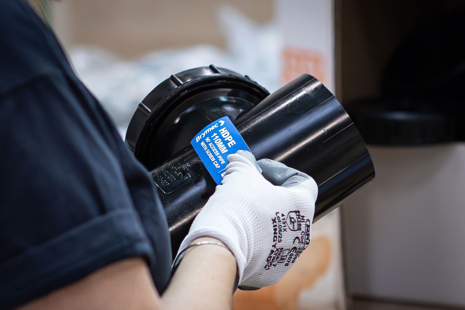 Person in white PPE gloves holding a black PVC pipe while adding a blue description sticker.