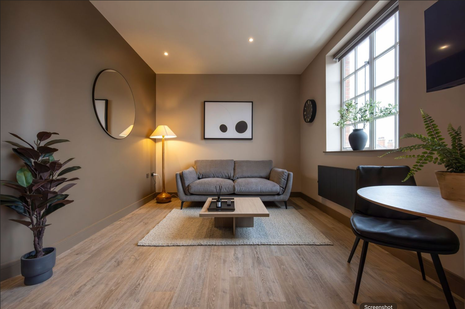 Modern minimalist bedroom interior with wood flooring, gray walls, and natural light from window.