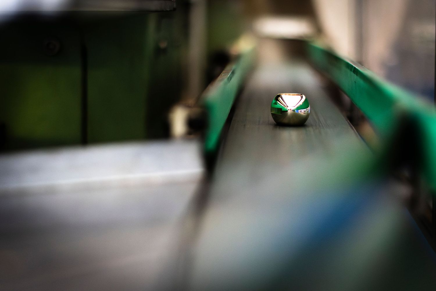 A small shiny brass valve part moving toward viewer along a conveyor belt with a soft focus background.