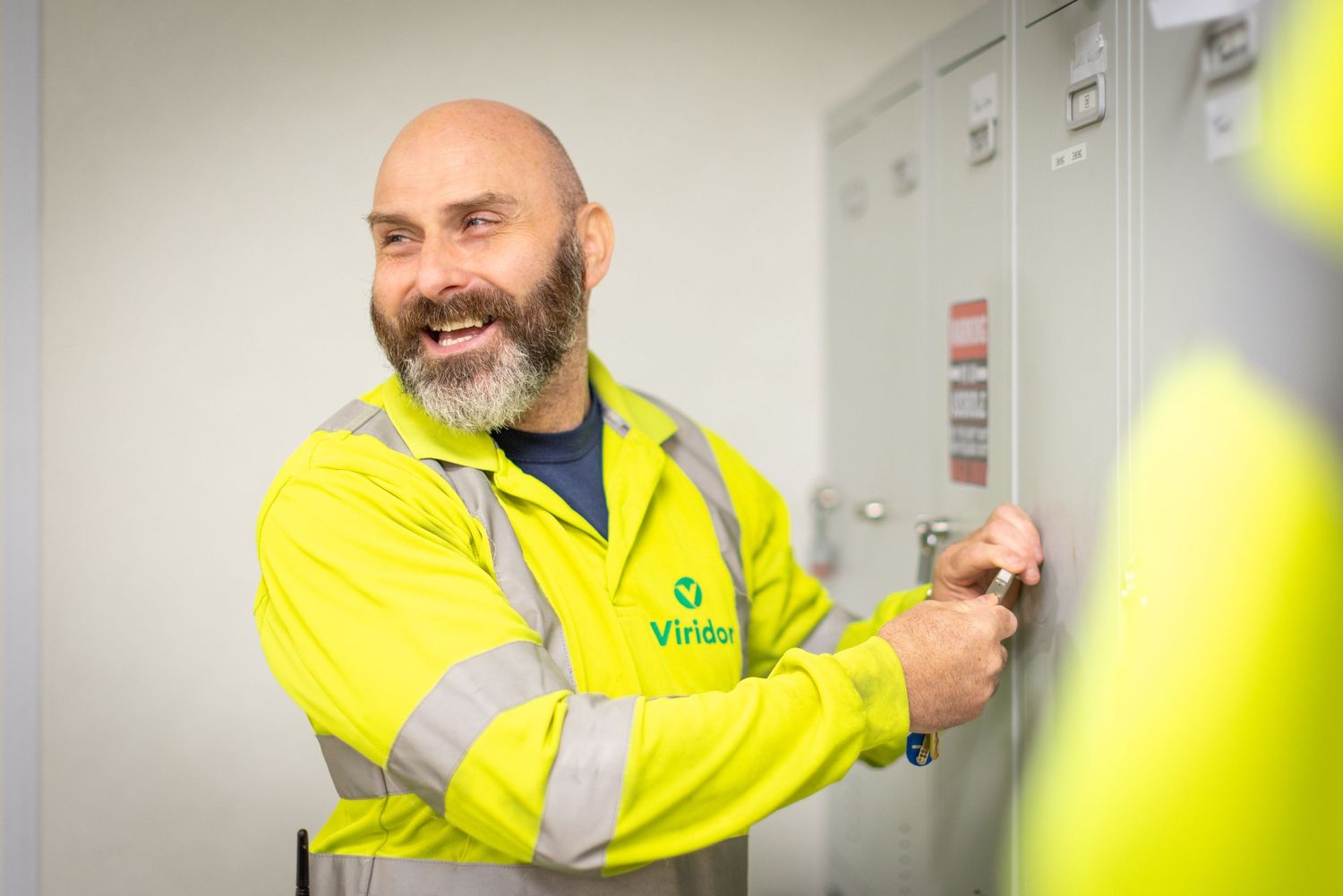 Worker in high visibility yellow safety jacket opens locker door in industrial setting.