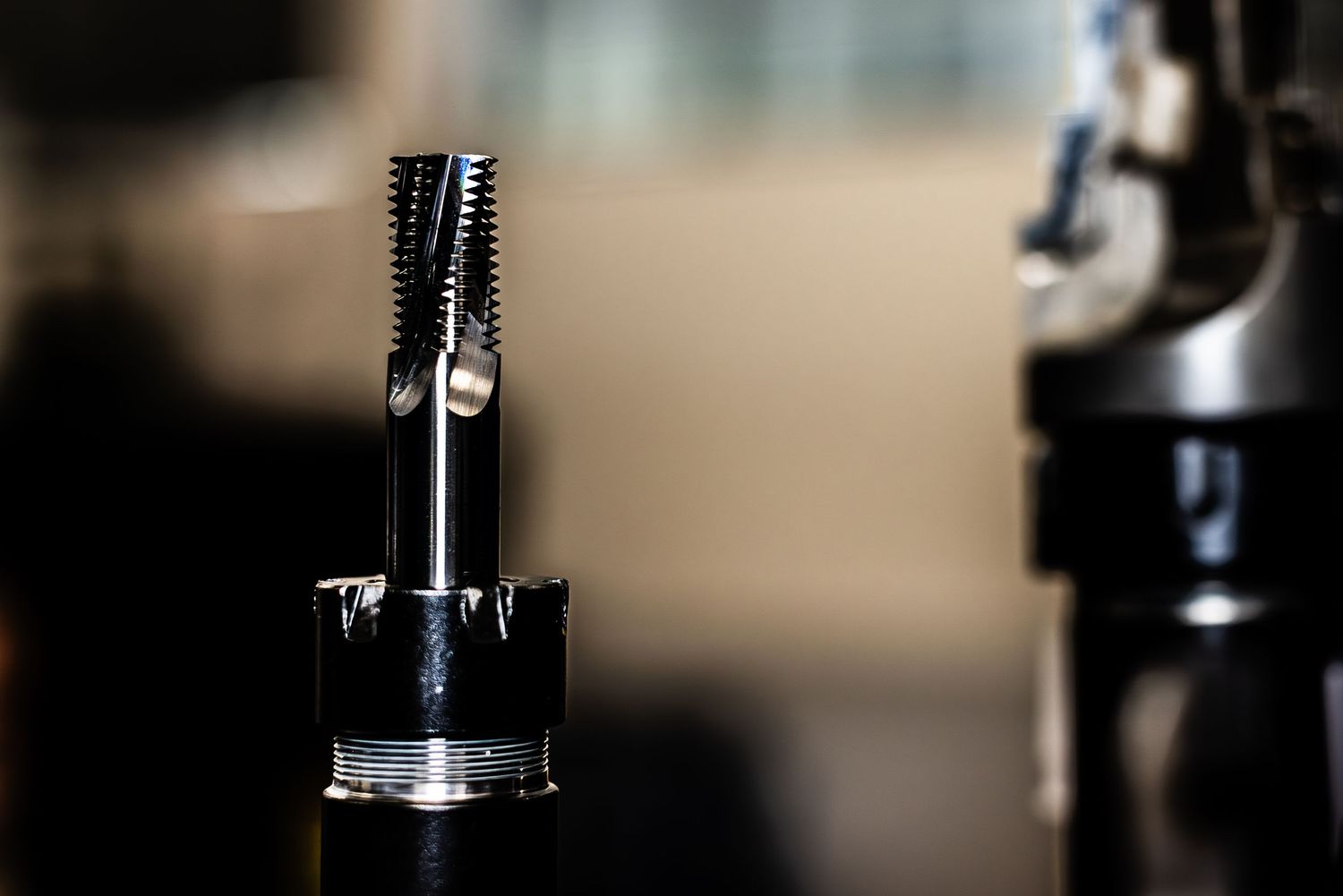 Close-up view of very sharp lathe tooling in dramatic low-key lighting against a soft-focus factory background.