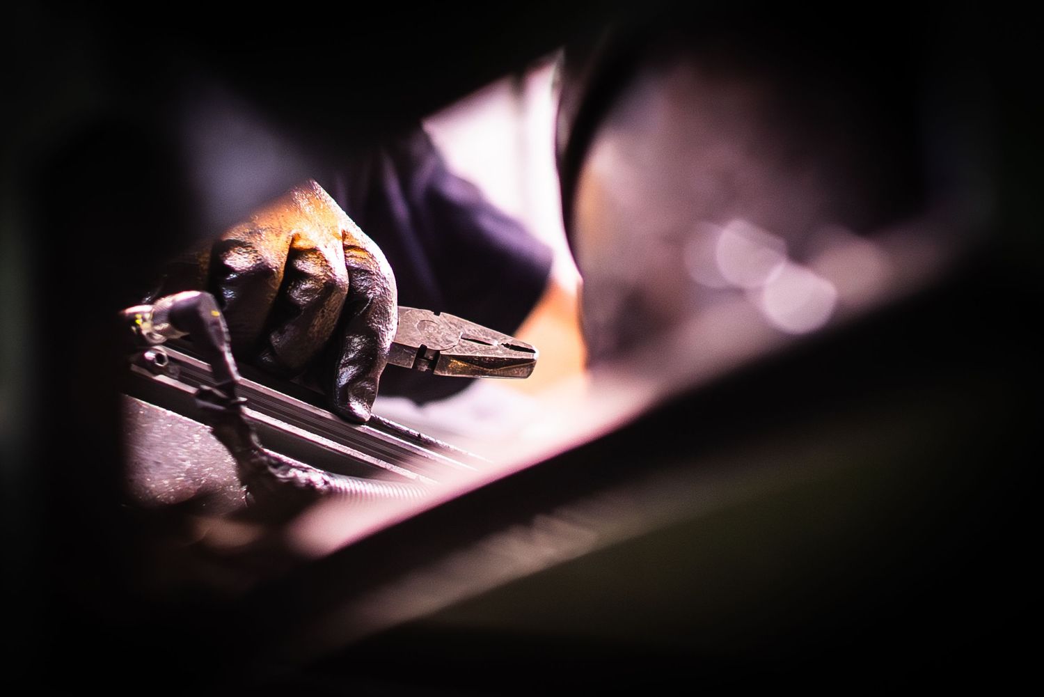 Dramatic photograph of gloved factory worker holding pliers working with forged metal valves in dramatic lighting.
