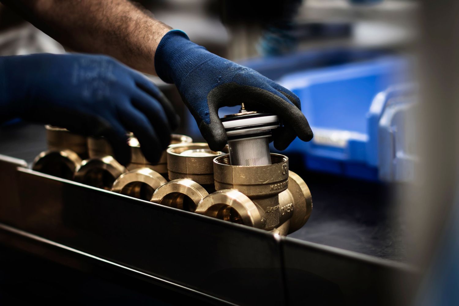 Close-up shot of hand selecting a brass valve off a workbench in manufacturing plant.