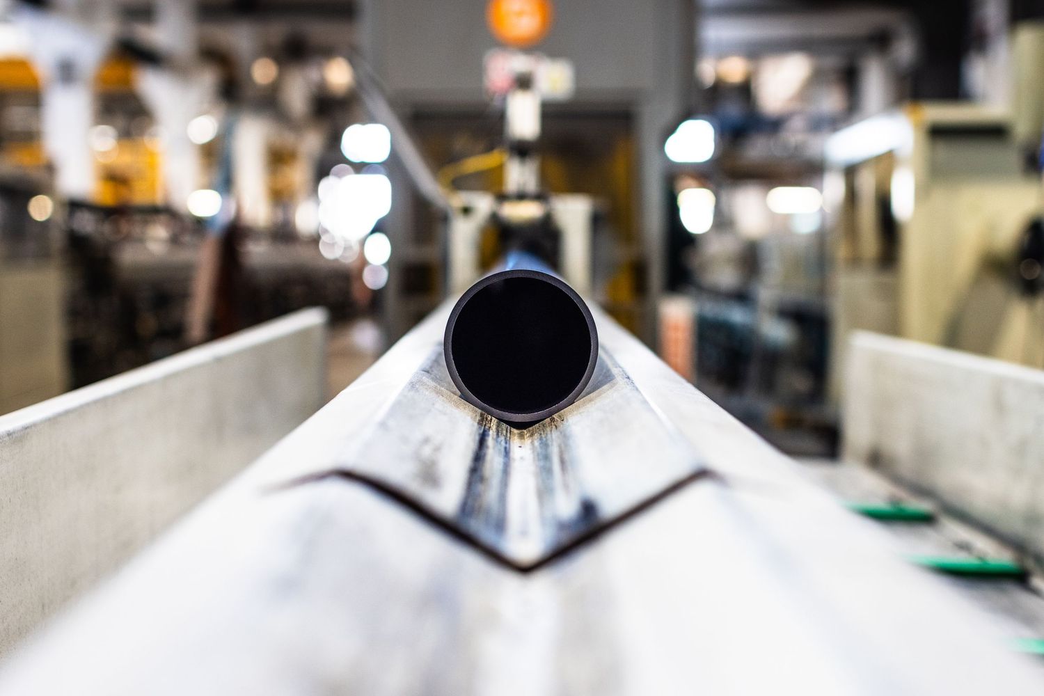 Black circular HDPE pipe slides towards viewer along a grooved channel in wide angle factory setting.