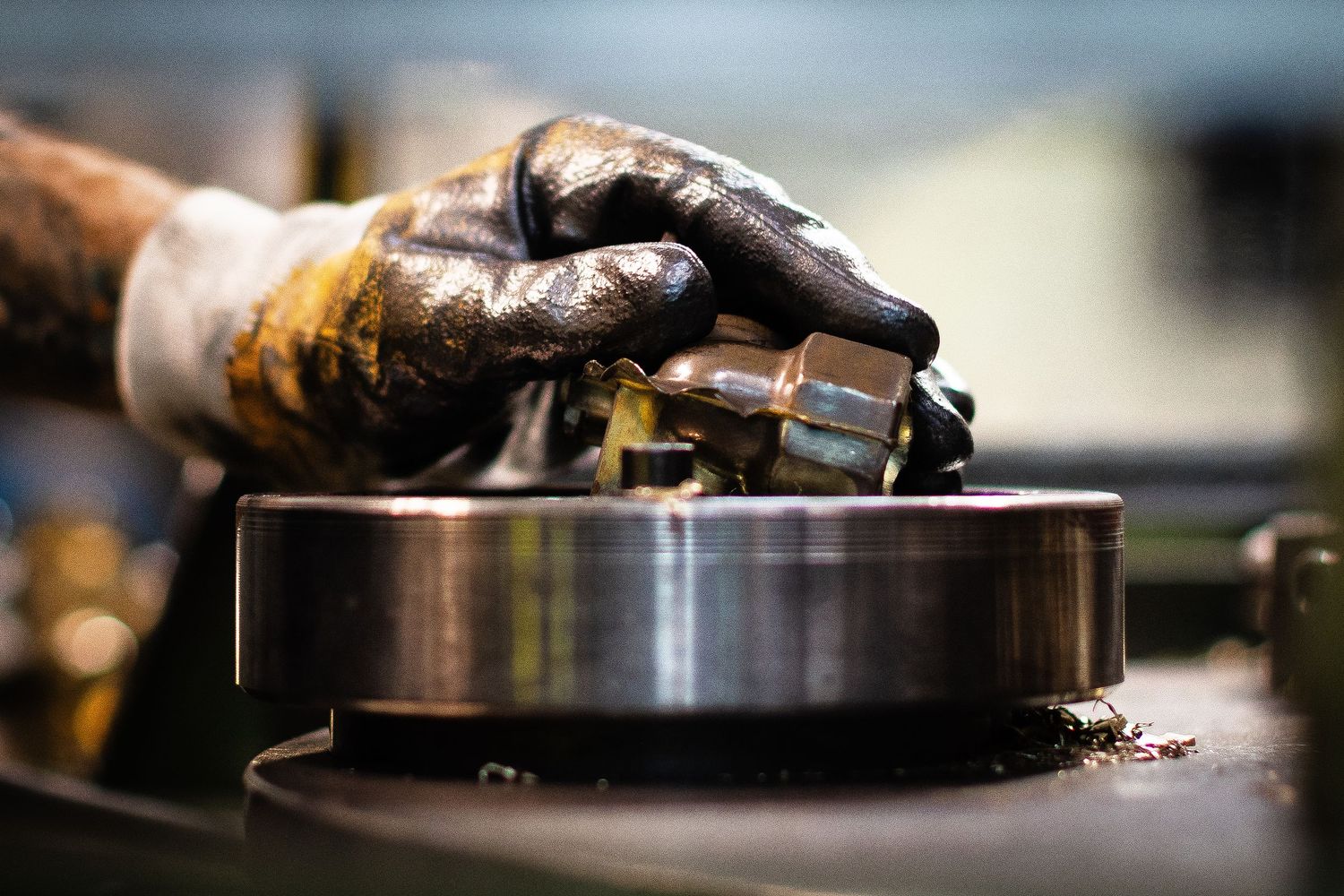 Close-up shot of gloved hand placing extruded metal valve casing on forged steel platform.