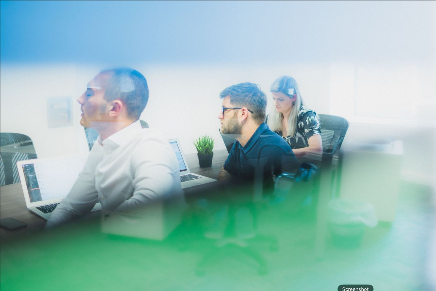 People working at computers in an office setting with a dreamy blue and green filtered effect.