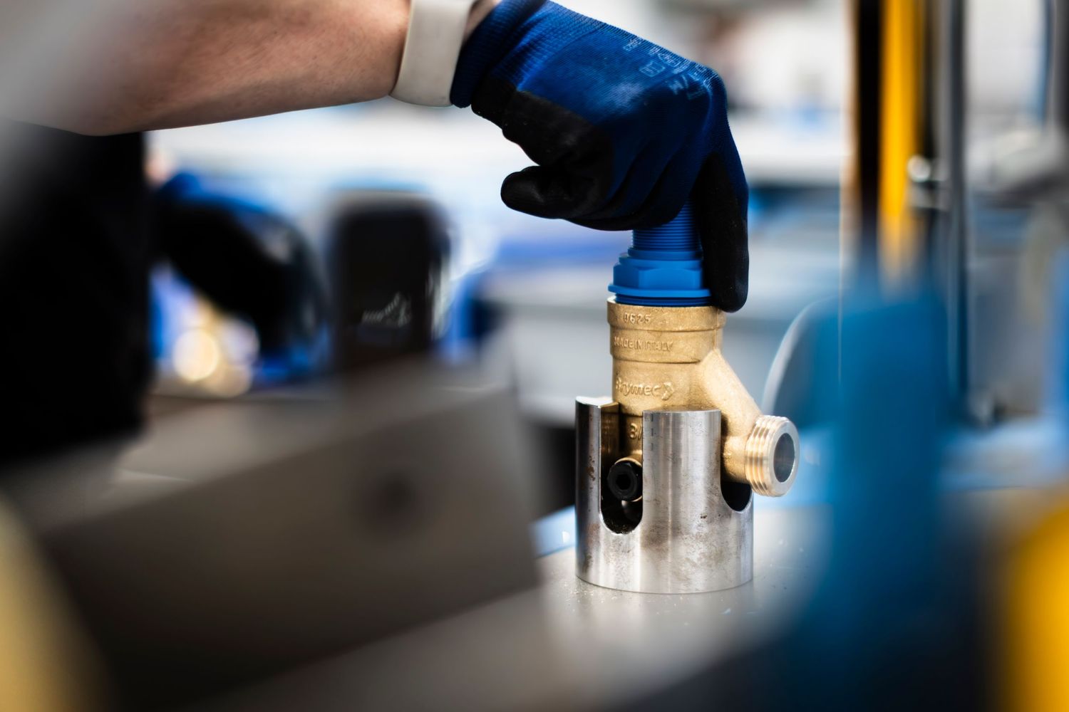 A gloved hand selects a valve being framed by soft focus industrial machinery in factory setting.