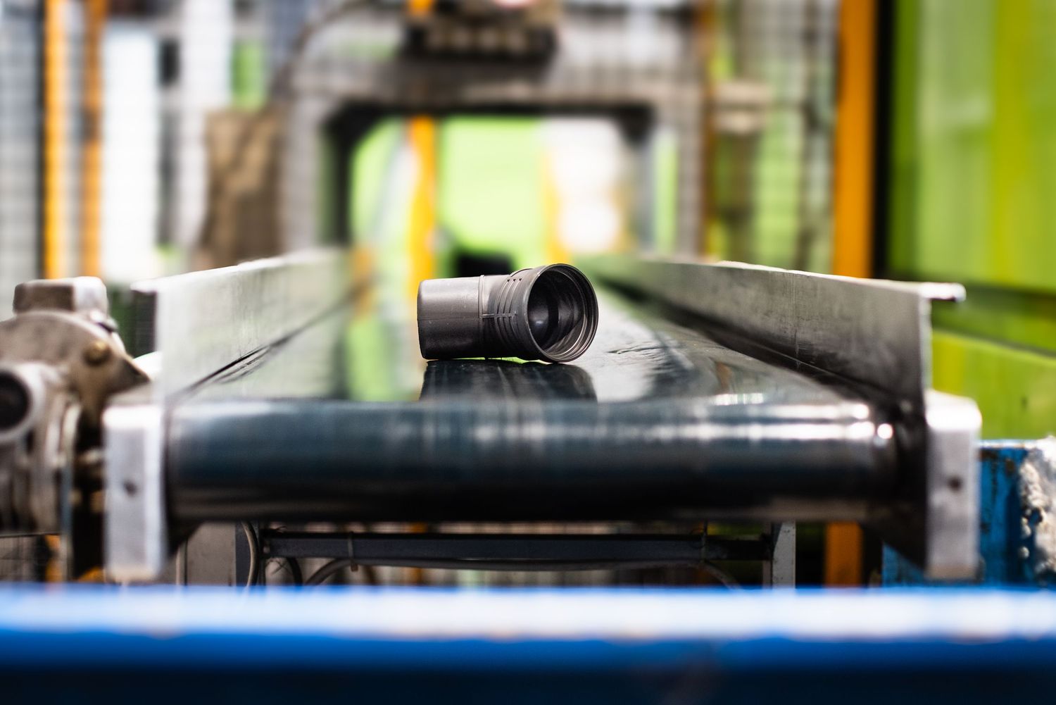 View of a small grey HDPE pipe moving toward viewer on conveyor belt in factory environment.