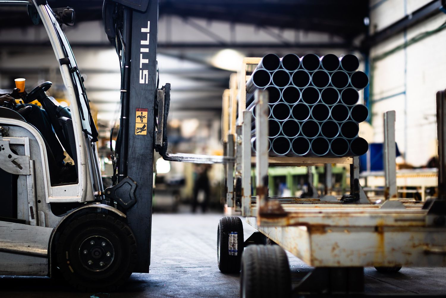 Industrial warehouse interior with a forklift stacked black HDPE pipes set against manufacturing equipment on concrete floor.