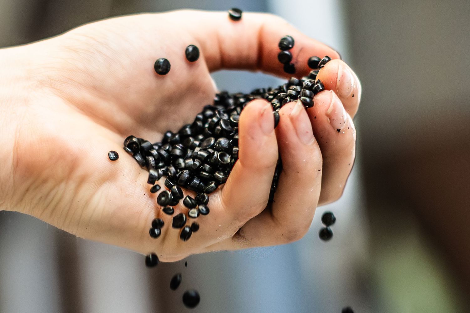 Hand holding black HDPE manufacturing pellets as they cascade and tumble.
