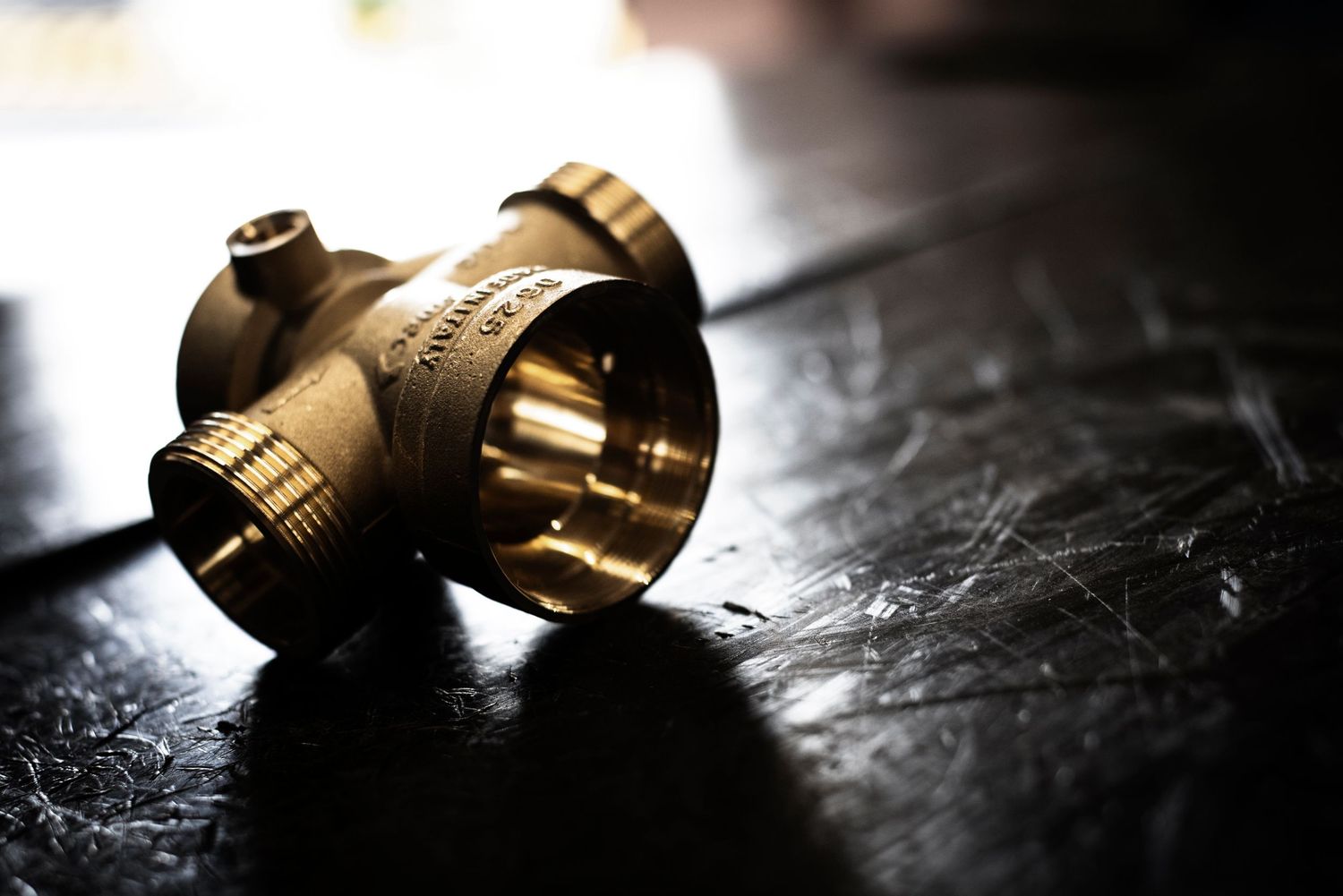 Brass plumbing valve fitting laying on dark a textured wooden surface with dramatic back lighting to create silhouette.