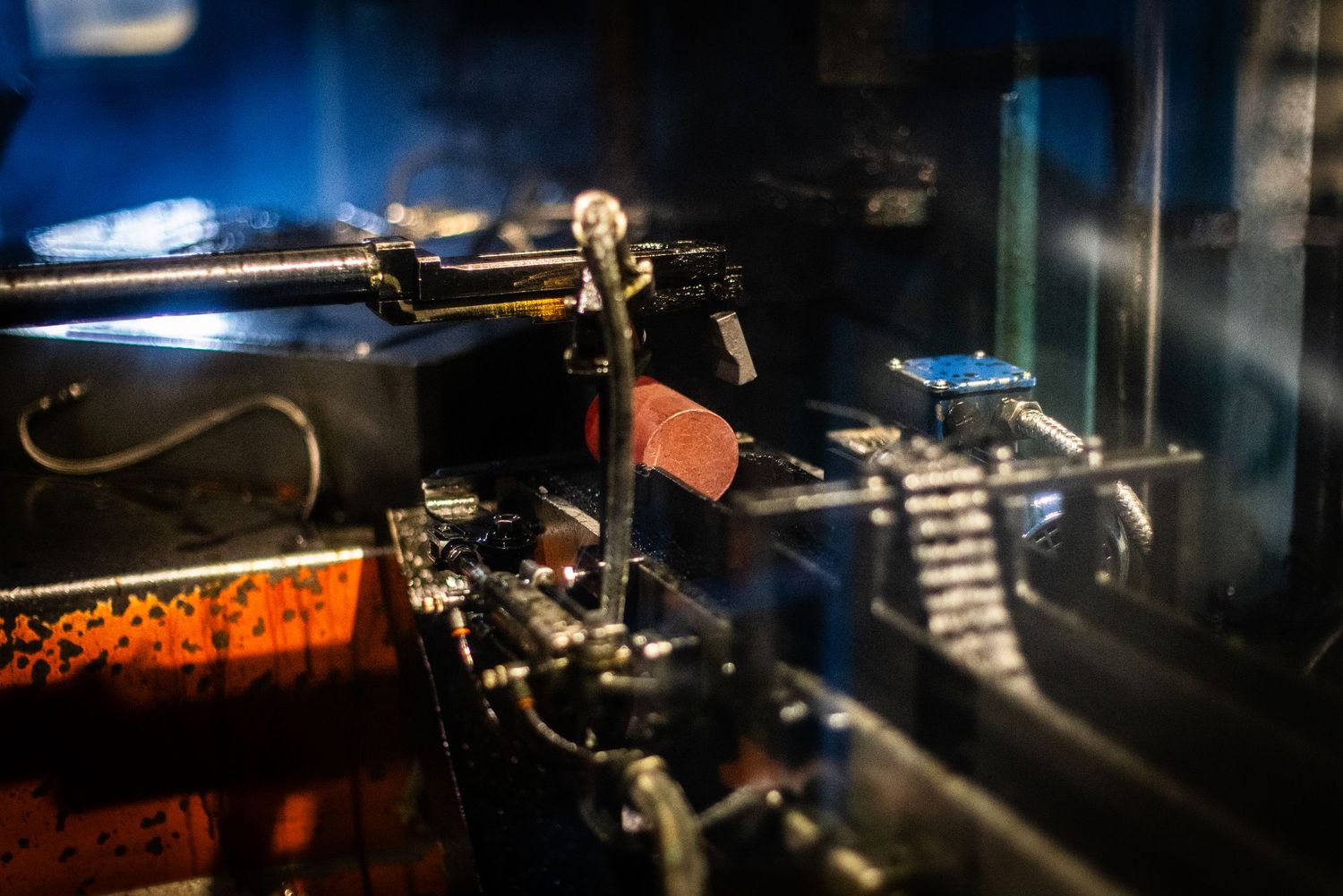 Heavy machinery about to forge glowing red steel cylinder into pipe in dark steamy setting
