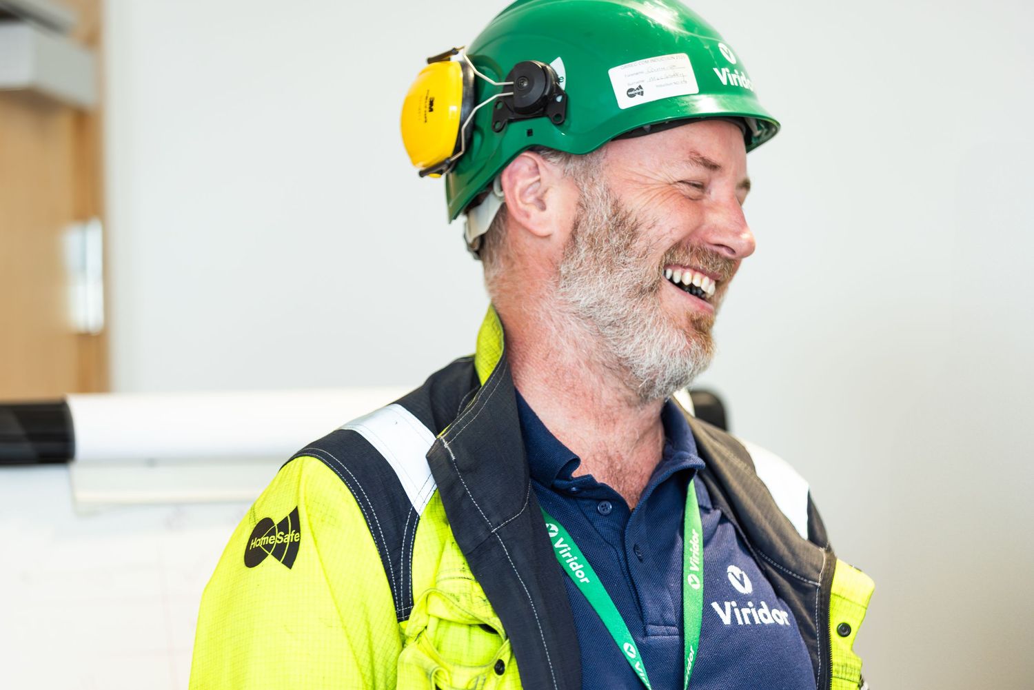 Construction workers in hard hats and safety vests smile while working together on a job site.
