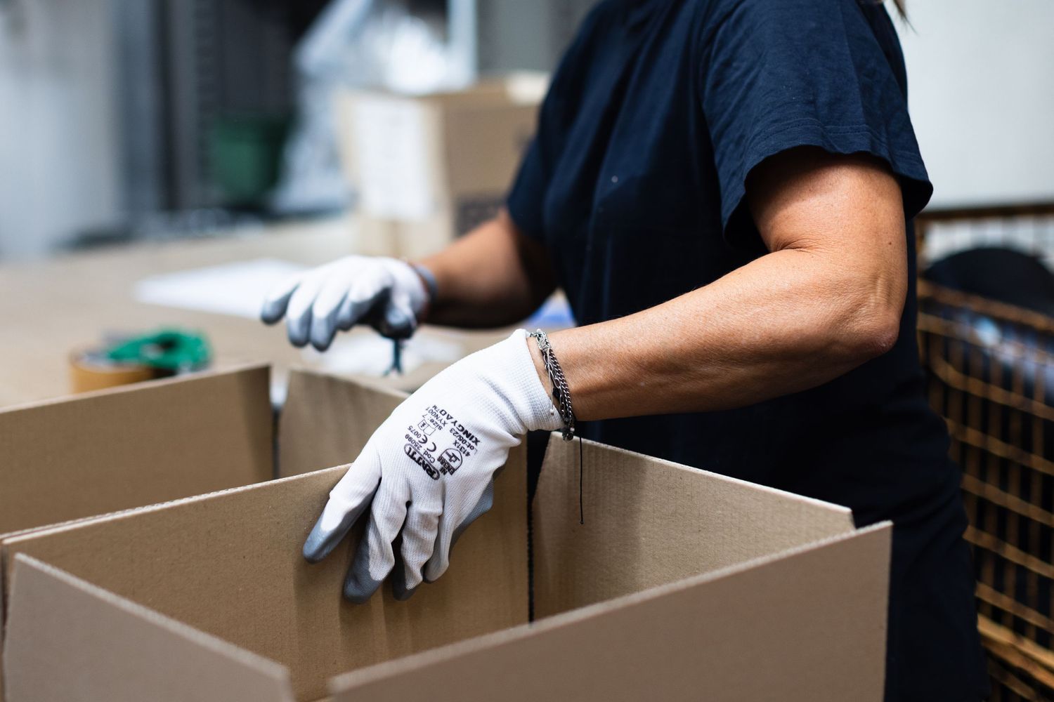 Worker in protective gloves packing cardboard boxes in a warehouse fulfillment center.