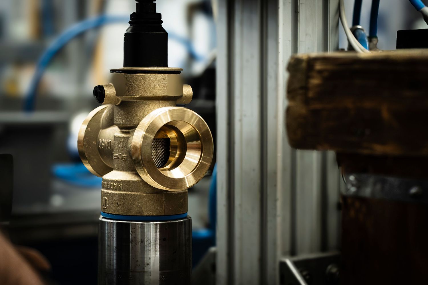 Close-up of a brass industrial valve or regulator component with blue pneumatic pipe in manufacturing setting.