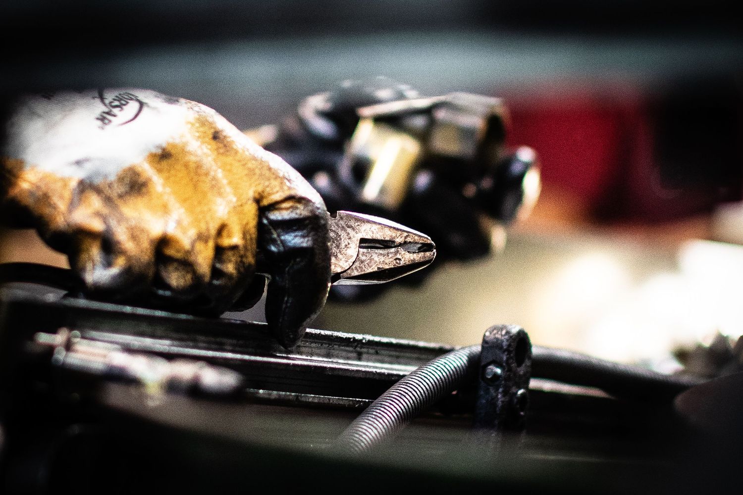 Close-up shot of a yellow-gloved factory worker cleaning edges of extruded metal valve casings in dramatic lighting