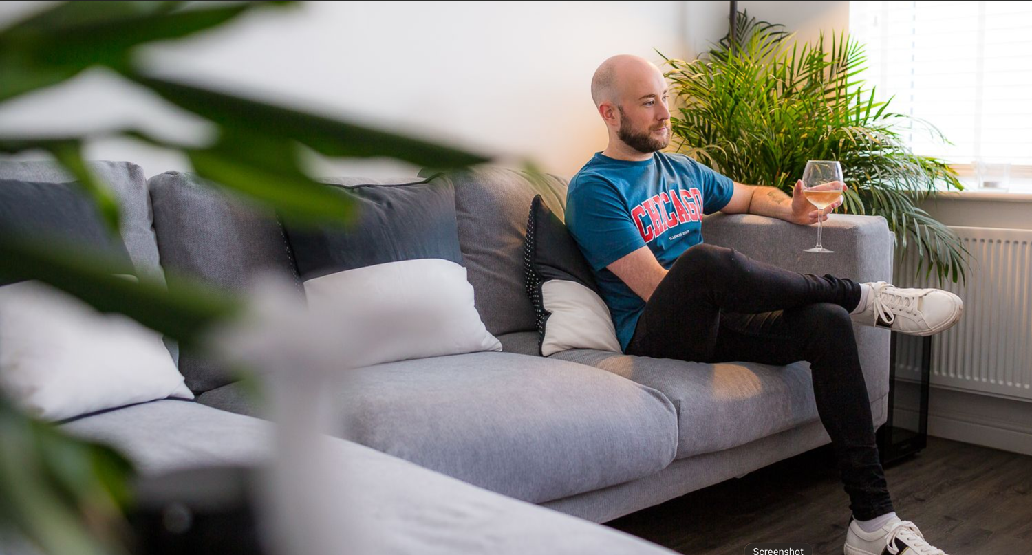 A person relaxes on a grey couch while using a laptop computer in a modern living room setting.