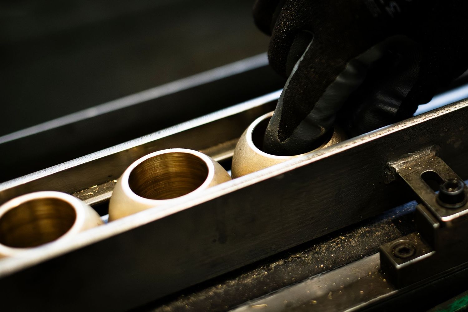 Close-up view of a gloved hand selecting brass valve components in a dark factory environment.