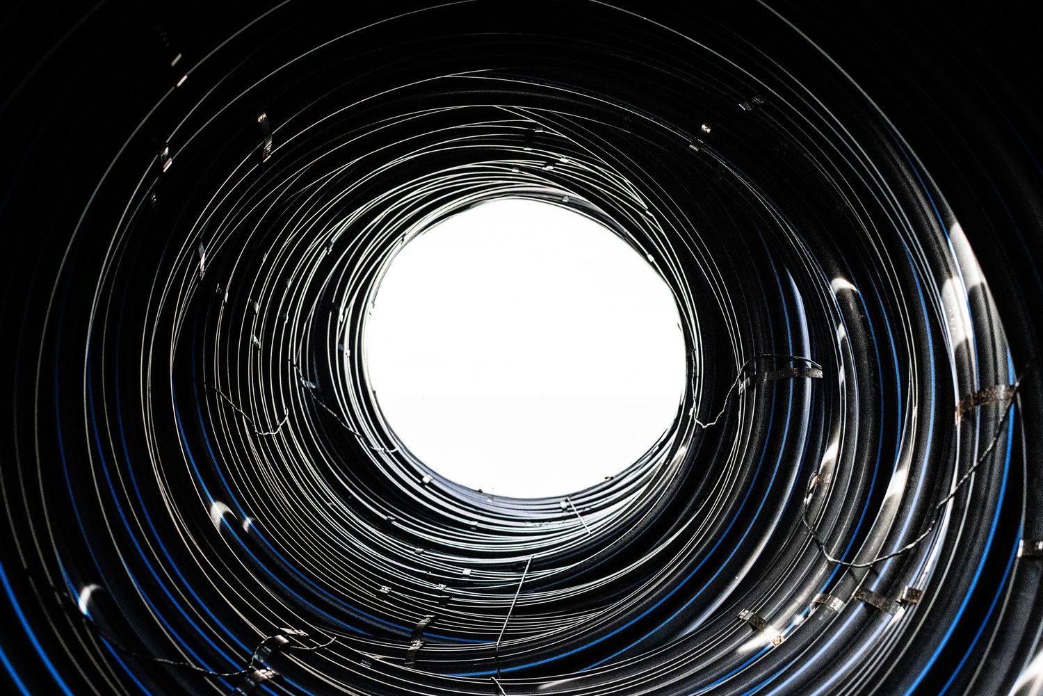 Dramatic view through huge circular roll of black HDPE pipes with dark sides and sunlight shining in from far end.