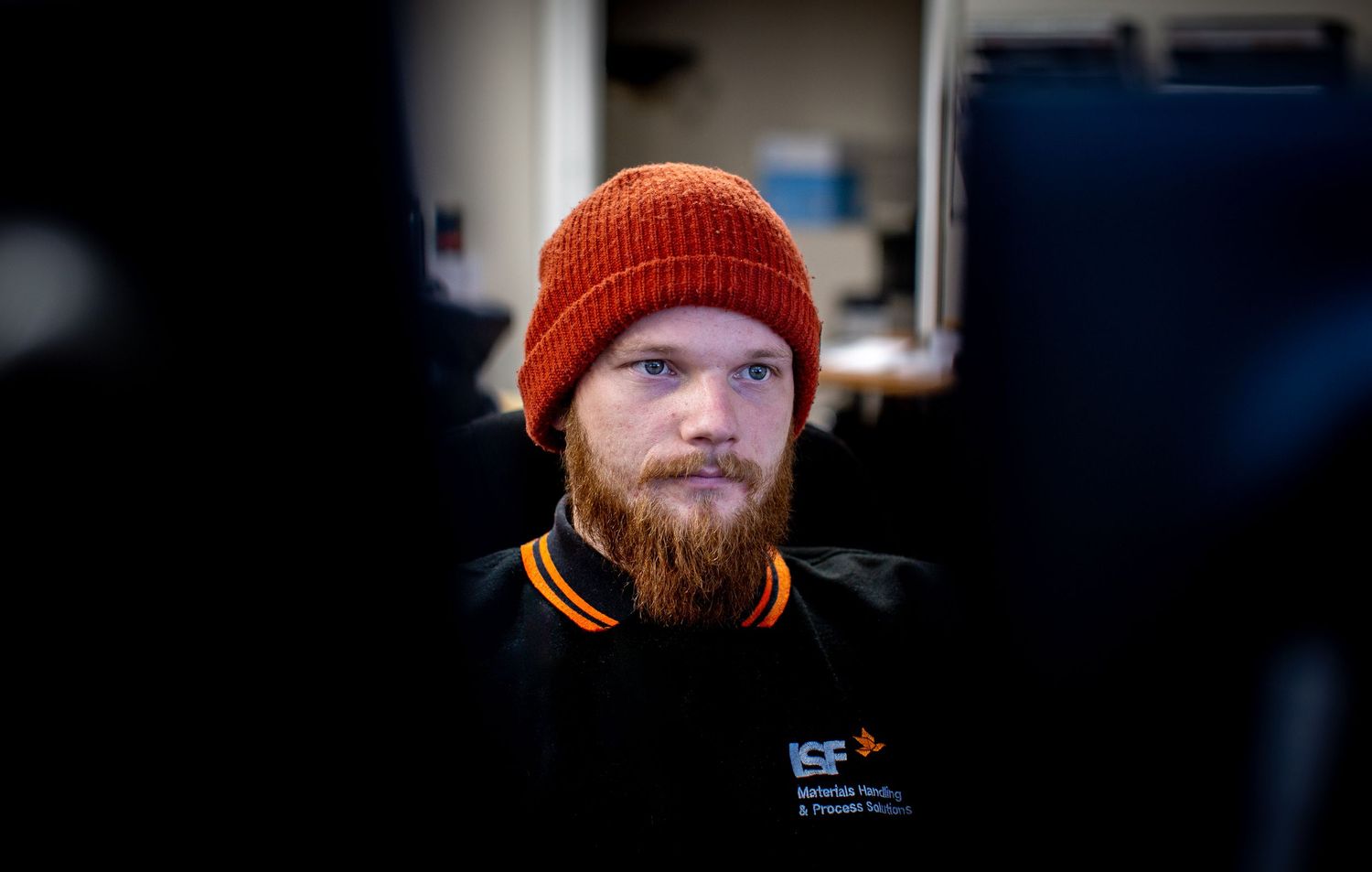 Person wearing an orange beanie and dark jacket in low light conditions with dramatic shadows.
