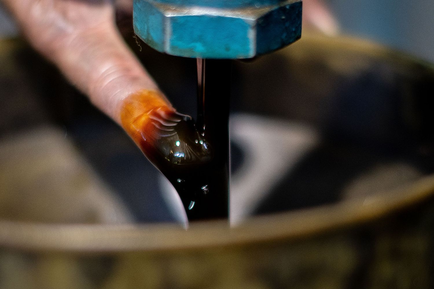 Close-up of a finger under a stream of dark oil pouring from a valve into a funnel.