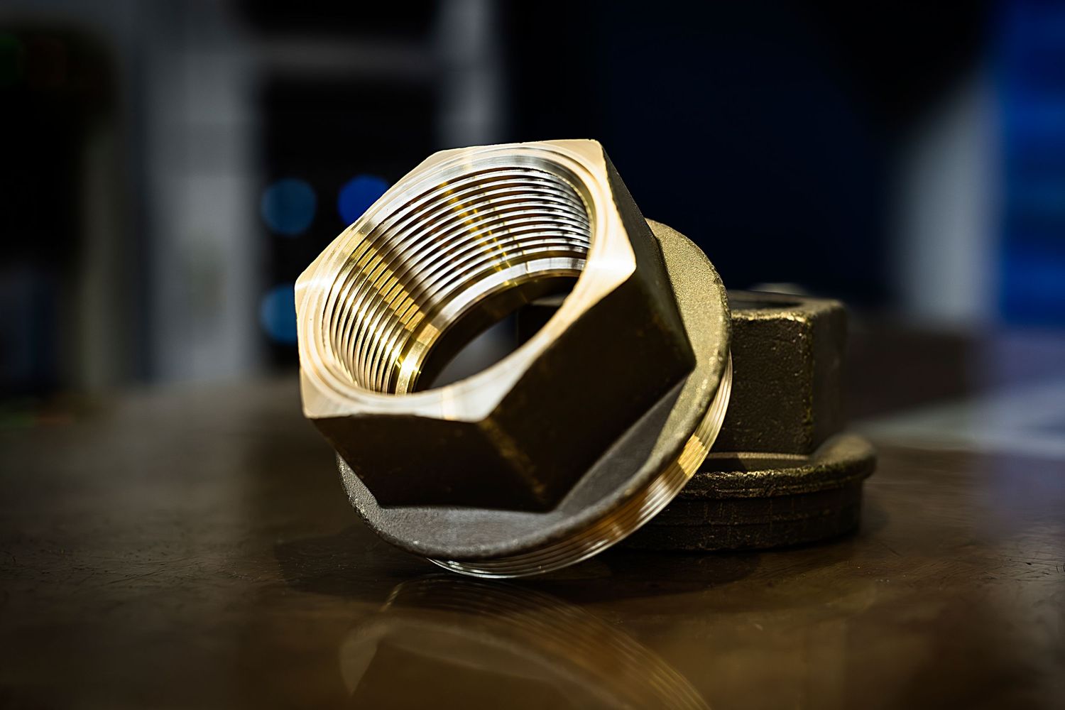 Close-up view of a very large brass hexagonal nut with shiny precision machined threads on dark surface.