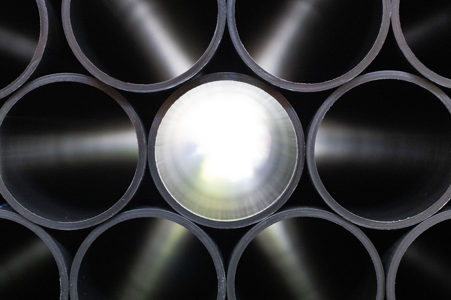 Industrial black HDPE pipes arranged in a circular pattern with sunlight steaming through to create reflections and lighting effects.