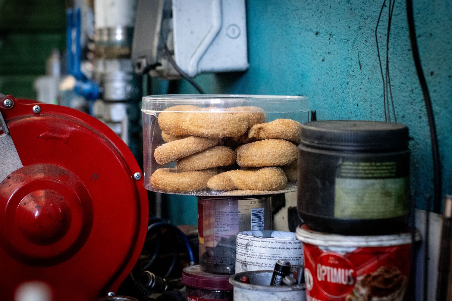 A clear plastic container tasty of stacked donuts sits among jars and tools on a factory workbench.