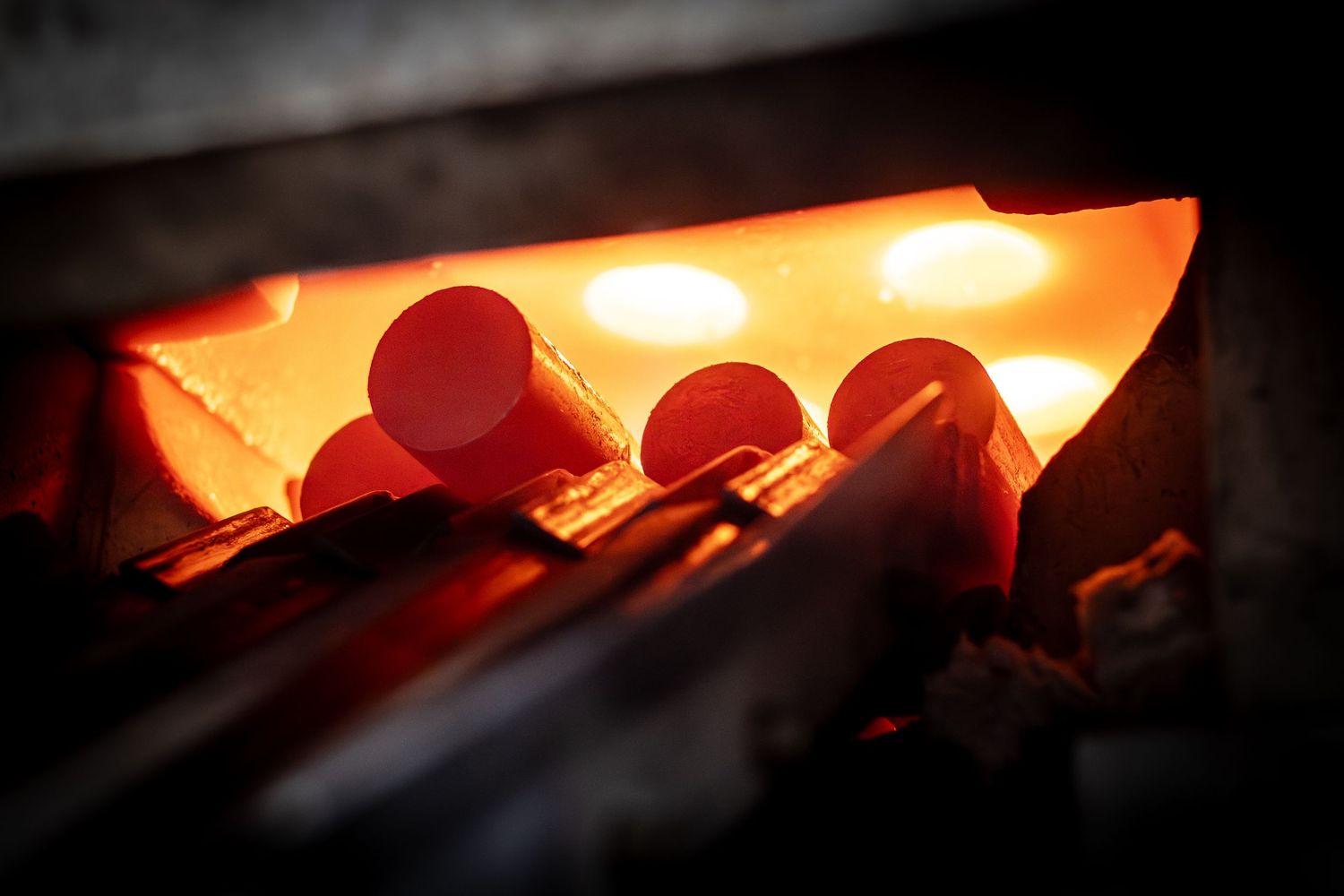 Glowing orange cylinders of steel emerging from intensely hot furnace.