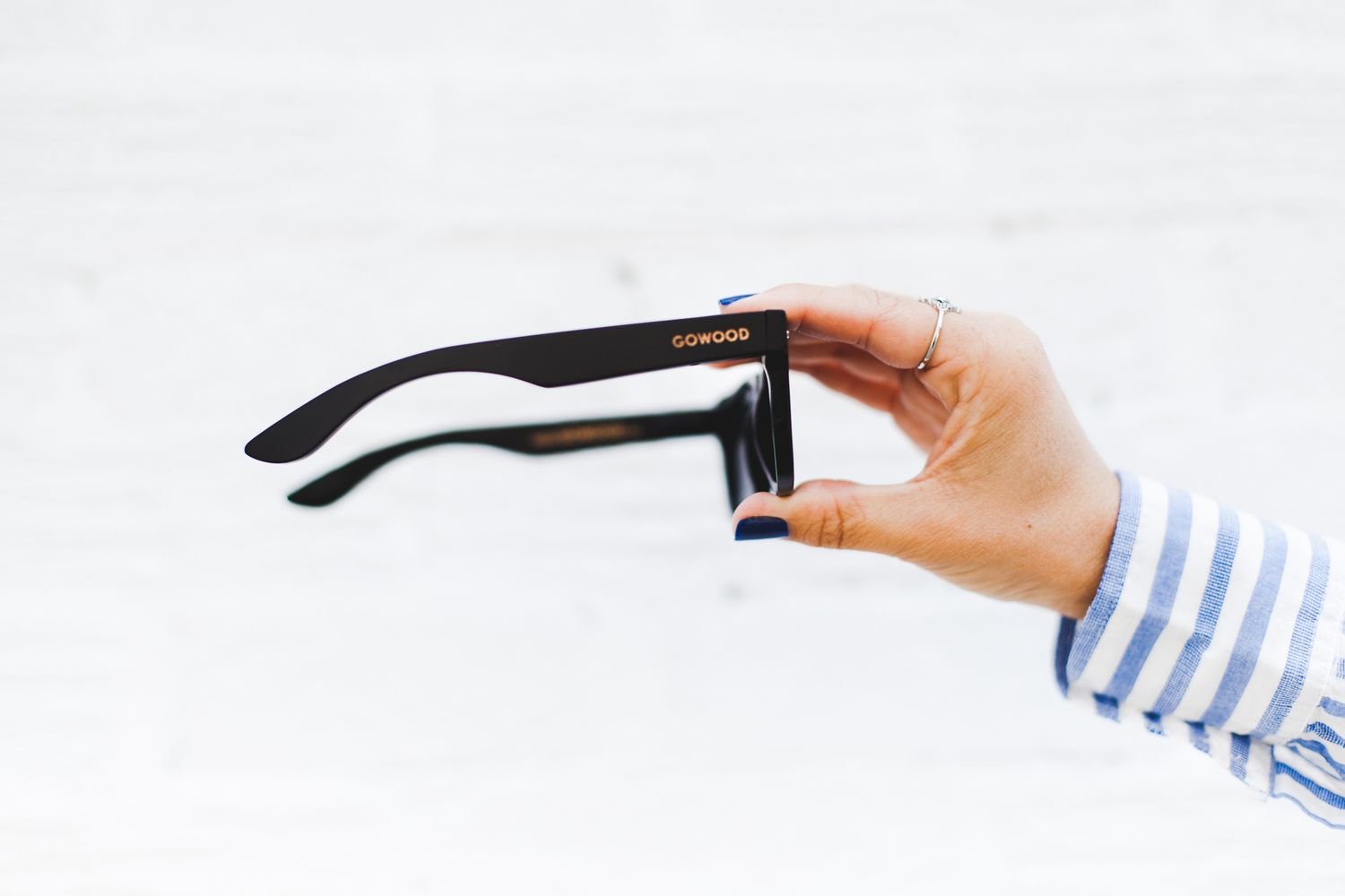 Hand holding black Sunwood sunglasses against white background wearing striped blue and white sleeve.