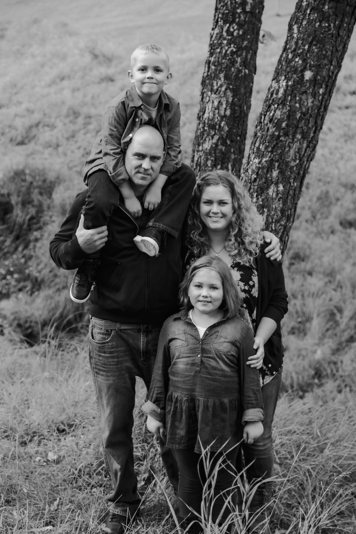 Black and white family portrait with two children near tree on grassy hill.