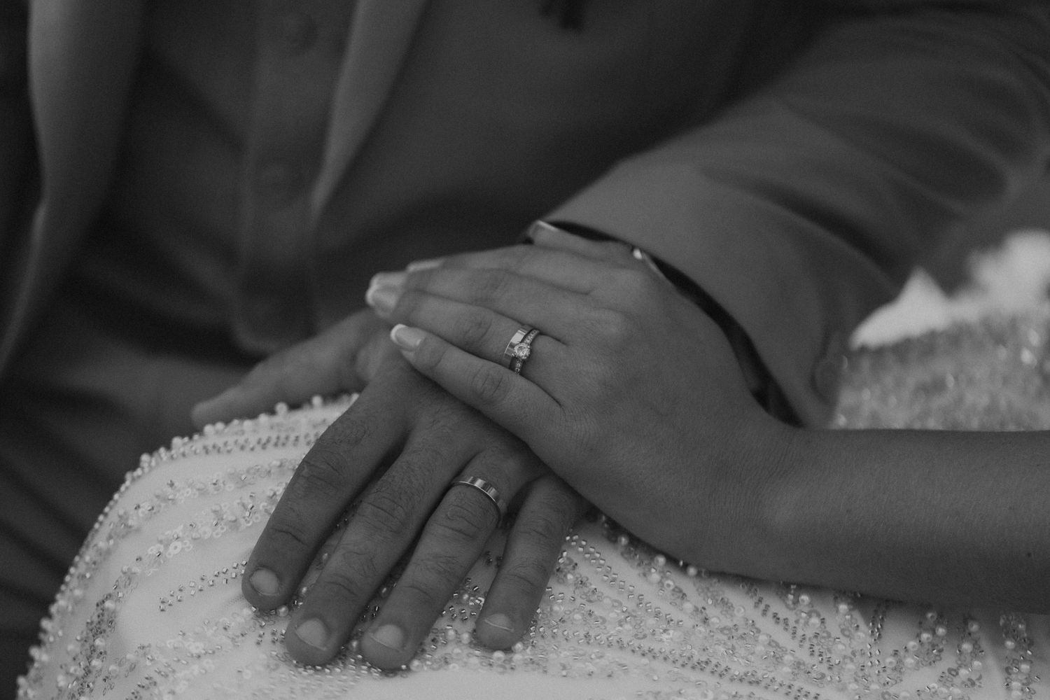 Close-up black and white shot of wedding rings and hands resting on white fabric.