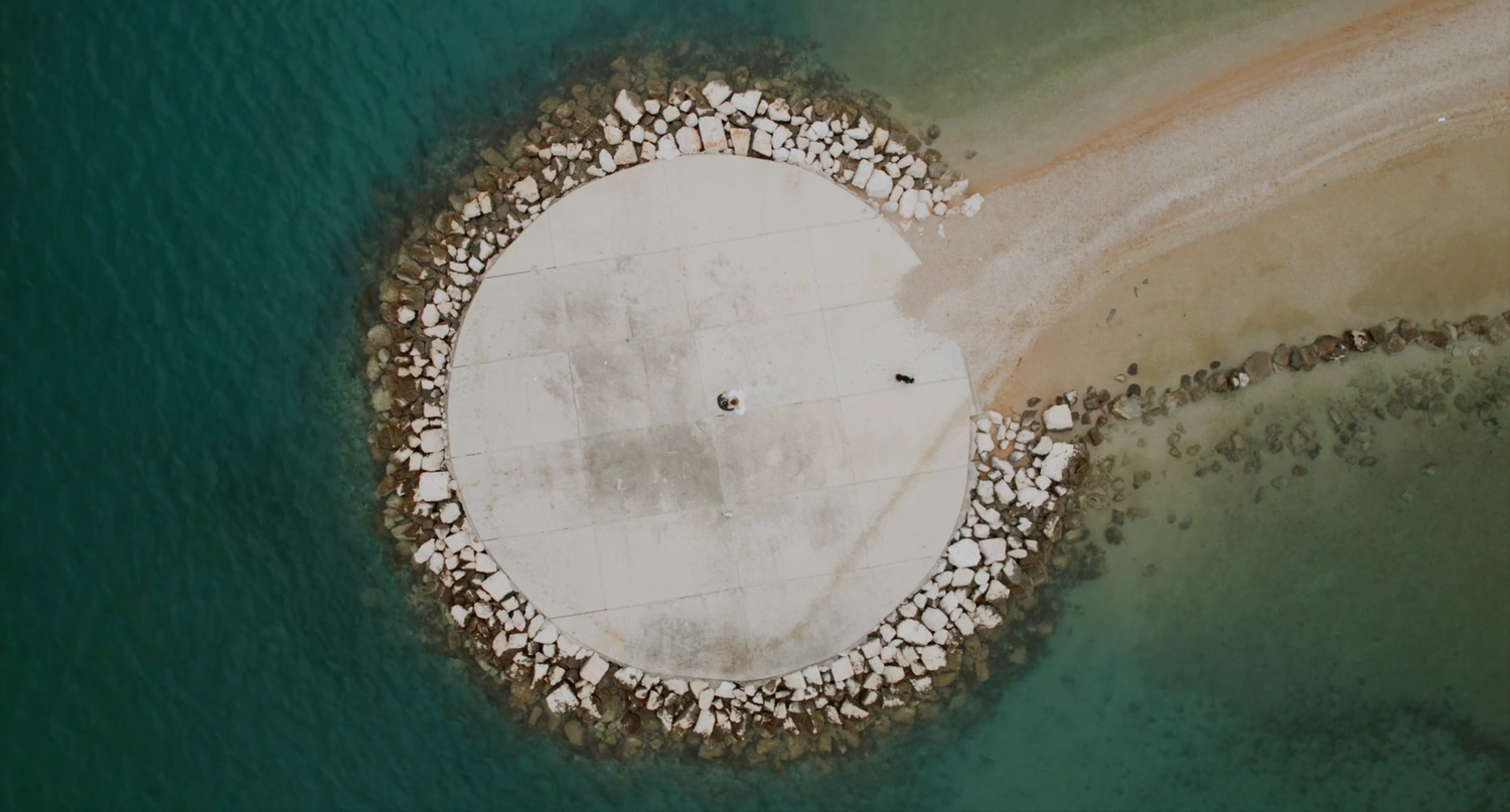 Aerial view of a circular concrete pier or breakwater surrounded by turquoise water.