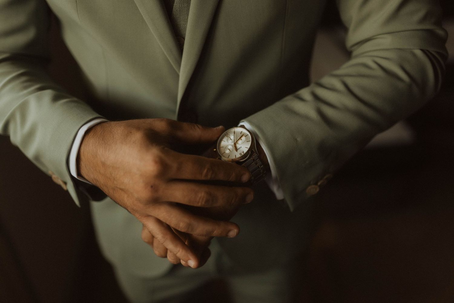 Close-up of hands wearing a formal olive suit jacket and wristwatch.