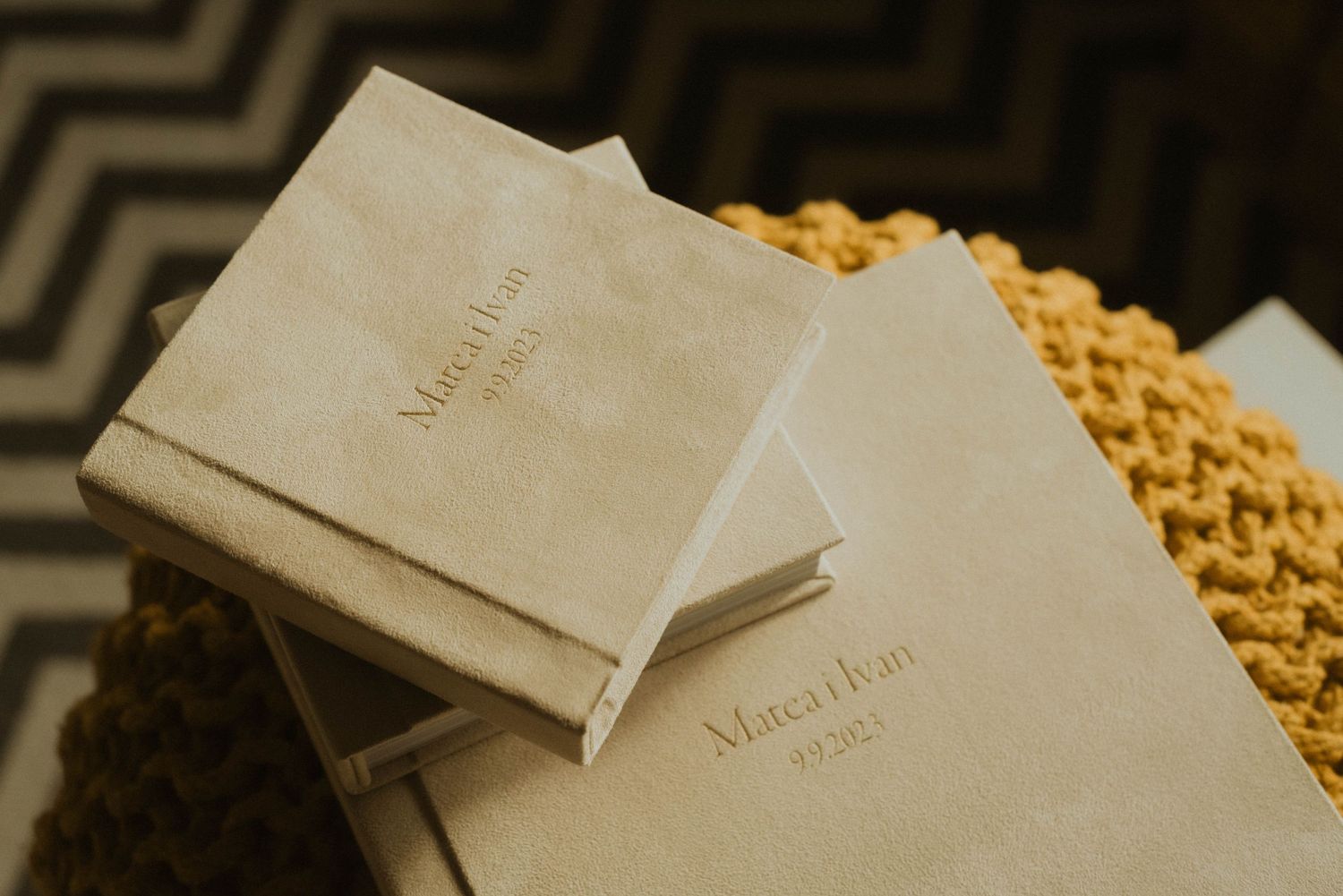 Wedding photo albums with embossed text stacked on a woven yellow surface.