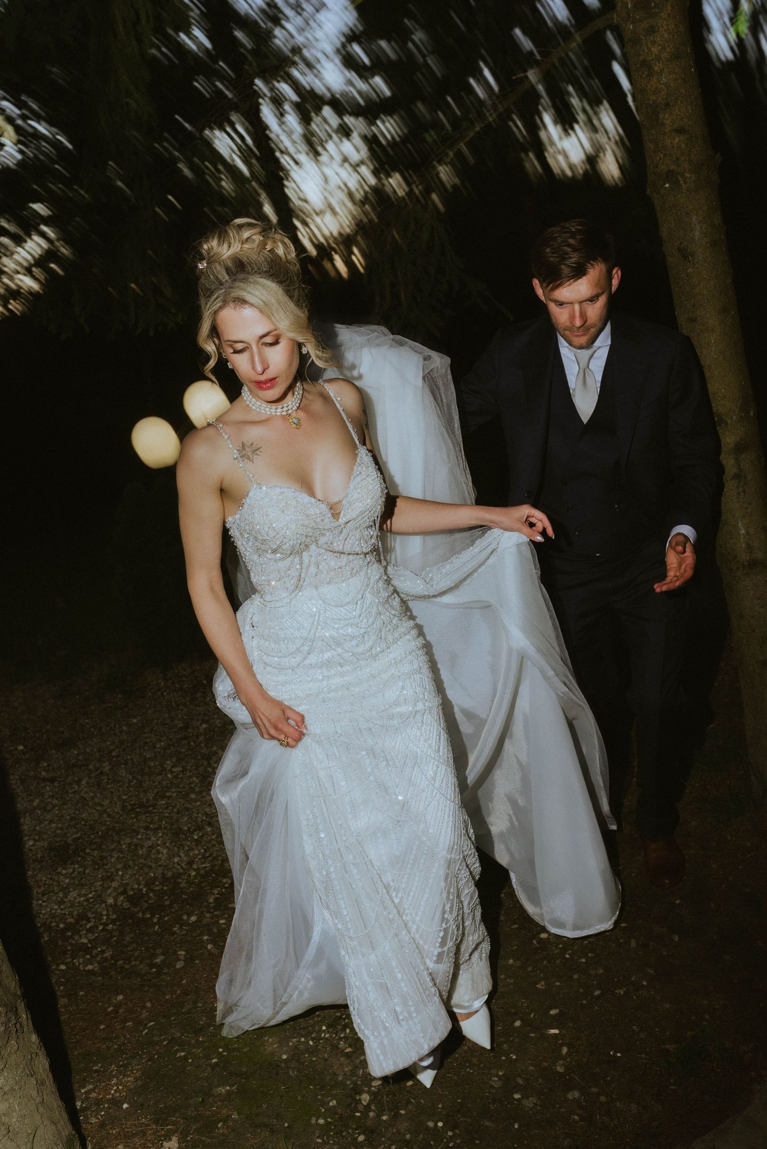 Artistic wedding photo of couple walking through dark forest at dusk.