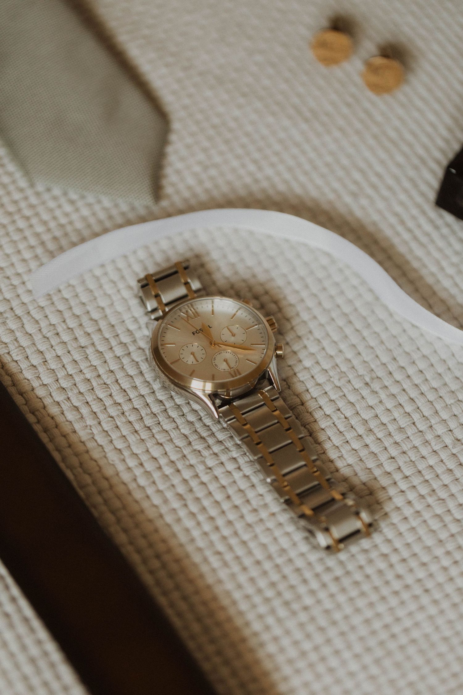 An elegant gold-toned wristwatch displayed on a textured white fabric background.