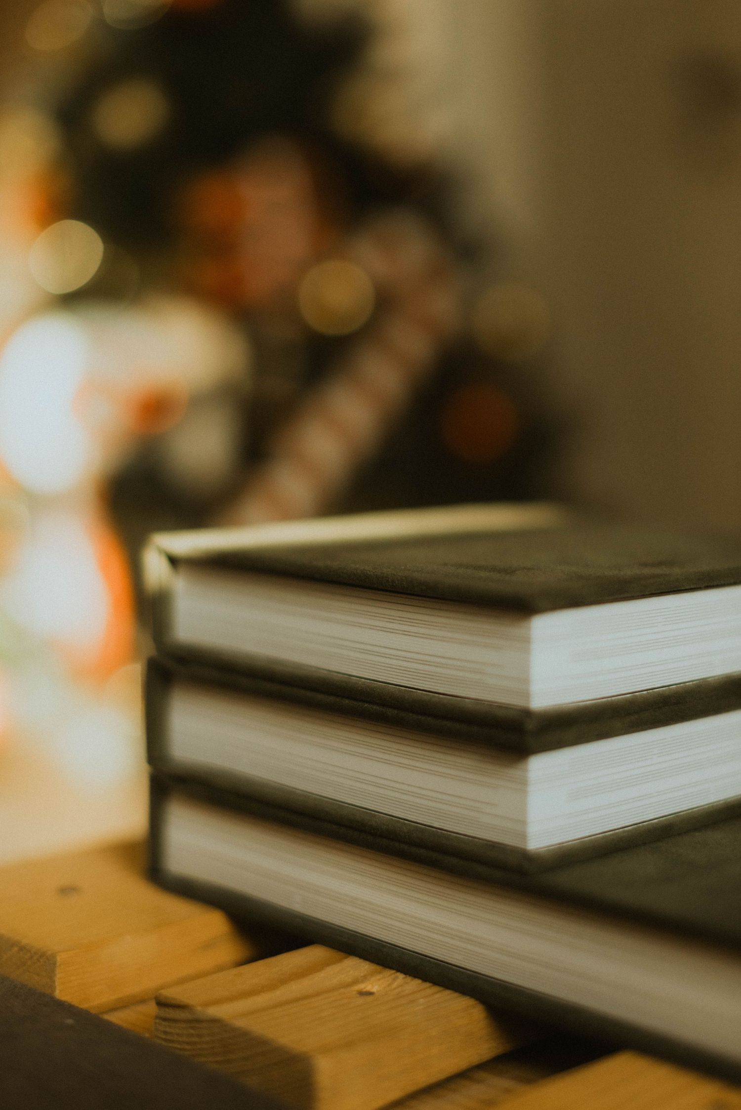 Stack of three hardcover books with blurred Christmas lights in the background.