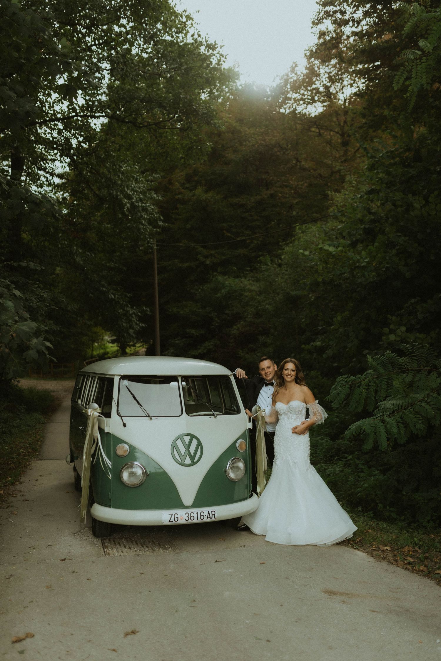 A classic mint green Volkswagen van parked on a forest path during a wedding photoshoot.