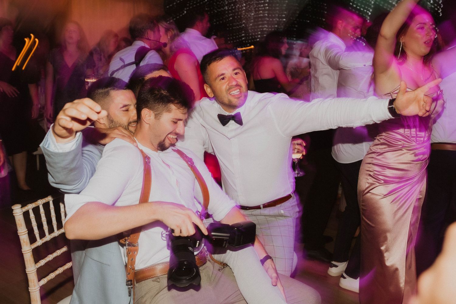 Wedding reception party guests dancing energetically under colorful lighting.