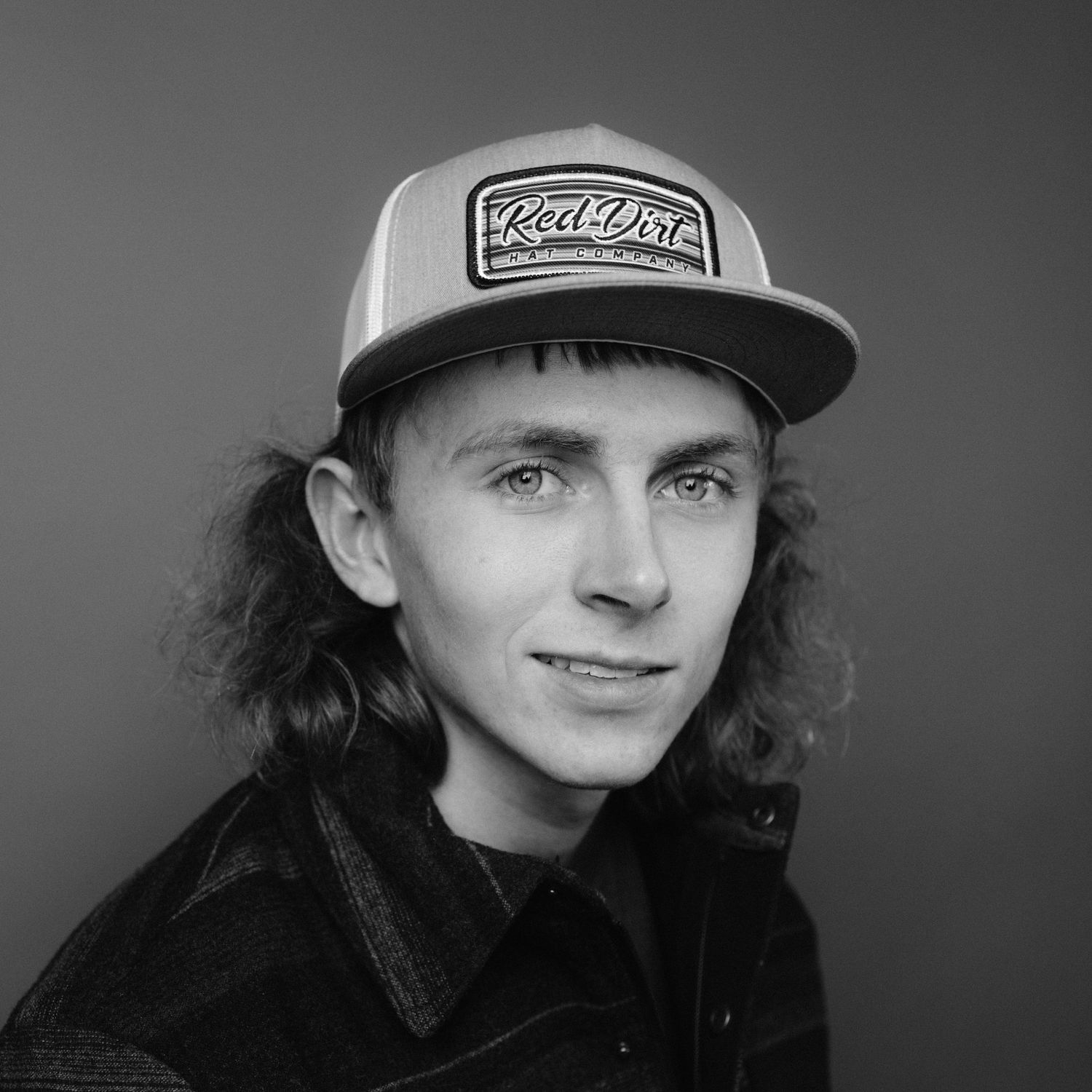 Black and white portrait of a young man wearing a Red Dot snapback cap with medium-length hair.