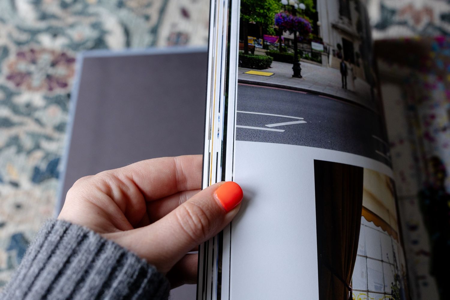 A hand flips through pages of a magazine or book against a floral patterned background.