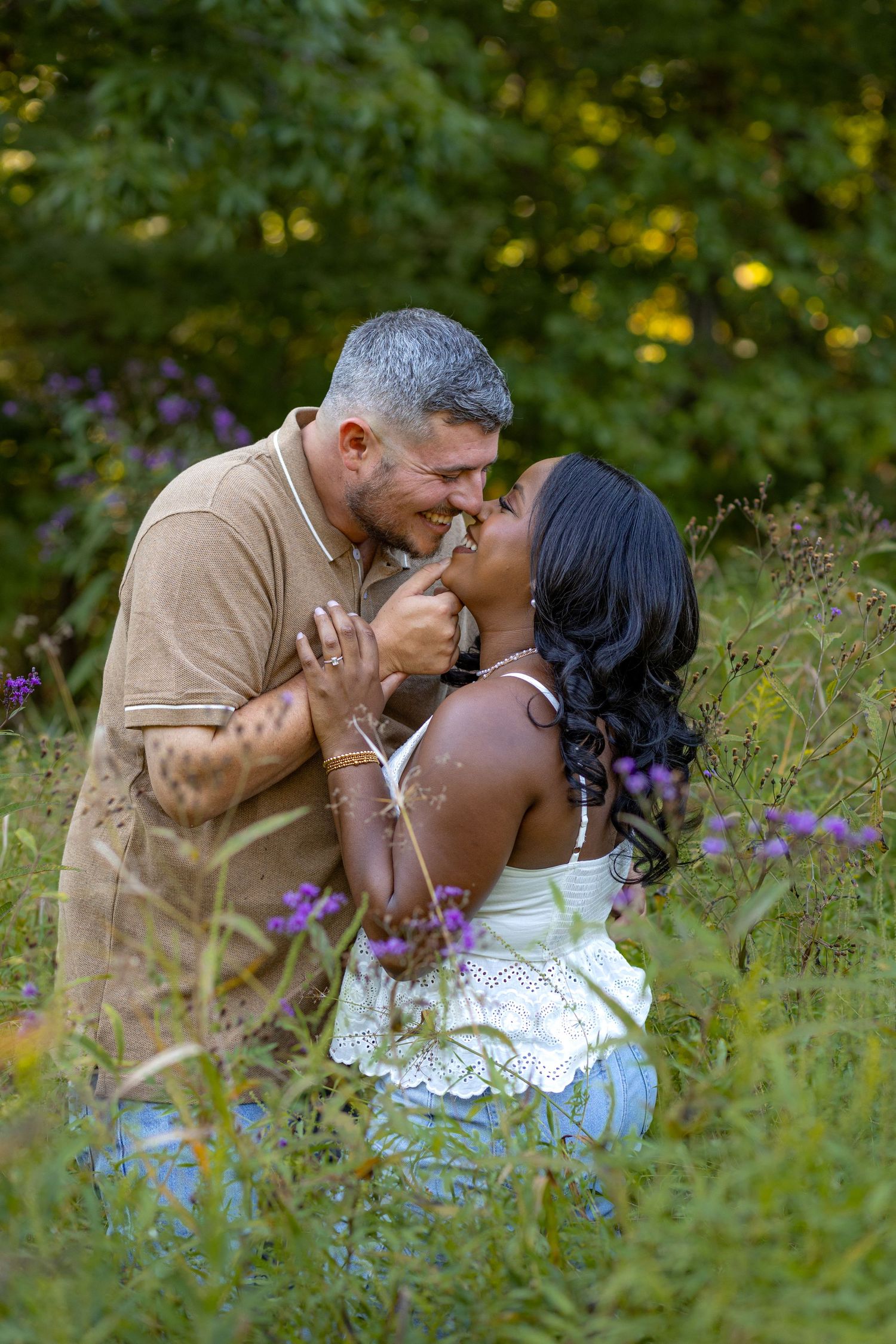 A couple shares an intimate moment among purple wildflowers in a sunny meadow.